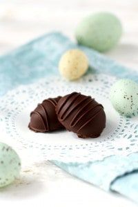 two chocolate eggs on a doily with speckled eggs in the background and one broken