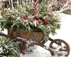 a wooden wheelbarrow filled with evergreens and red berries in the winter snow