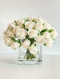 a bouquet of white roses in a square vase on a counter top with water droplets