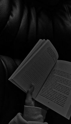 a person is reading a book while sitting in a leather chair with their hand on the open book