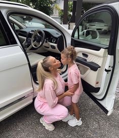 two women in pink outfits sitting next to a white car with the door open and one woman touching her lips