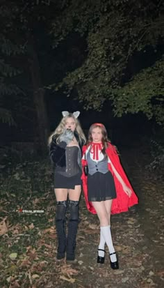 two women dressed up in costumes standing next to each other on a forest path at night