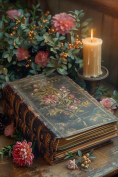 an old book sitting on top of a table next to flowers and a lit candle