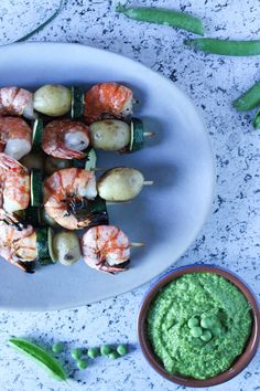 shrimp and vegetable skewers on a white plate next to a small bowl of guacamole