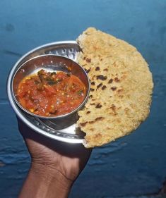 a hand holding a metal bowl with food in it next to a piece of bread