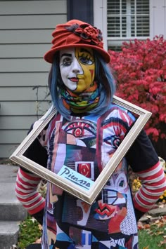 a person with painted face and body holding a framed photo in front of a house