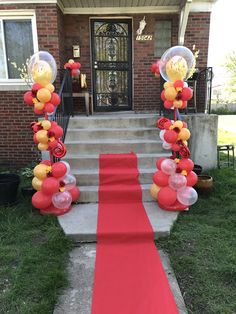 a red carpeted walkway with balloons and streamers on the steps leading up to a house