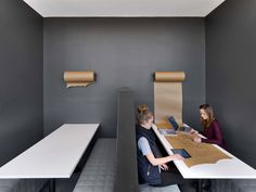 two women sitting at a table with laptops in an office space that is painted gray