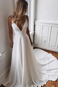 a woman in a white wedding dress standing by a window with her back to the camera