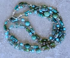 This terrific 2-Strand Necklace displays an impressive number of Turquoise and Czech Glass elements, paired with Sterling Silver. There are 33 discrete components in the design, in a multitude of blue, green and silver hues. A veritable treasure trove of styles. While the 33 styles are too many to elucidate, some notable elements include: Striking Czech Faceted Saucers in appealing Picasso turquoise hues Classic blue Turquoise Ovals with distinctive dark brown matrix Glossy light and dark green Necklace Displays, Southwest Design, Green And Silver, Green Peridot, Tube Beads, Heart Beads, Green Turquoise, Toggle Clasp, Strand Necklace