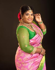 a woman in a pink and green sari posing for the camera with her hand on her hip