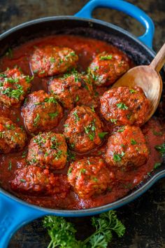 meatballs in tomato sauce with parsley on the side and a wooden spoon sitting next to it