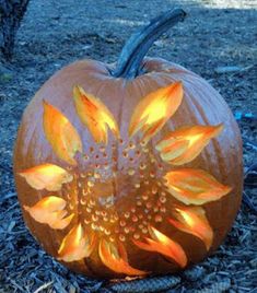 a carved pumpkin with yellow flowers on it sitting in the grass next to some leaves