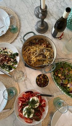 a table topped with plates and bowls filled with food next to wine bottles on top of a marble counter