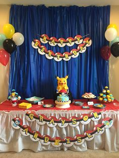 a pokemon birthday party with balloons, cake and decorations on a table in front of a blue curtain