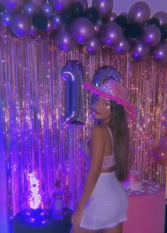 a woman wearing a white dress and pink hat standing in front of balloons with the number one on it