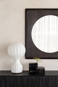 a white vase sitting on top of a black dresser next to a mirror and lamp