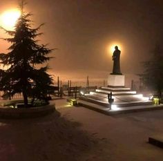 a statue is lit up in the snow at night