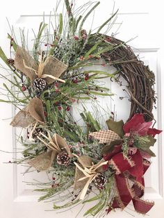 a christmas wreath with pine cones and red ribbon hanging on a white front door decorated for the holiday season