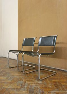 two black chairs sitting next to each other on top of a wooden floor in front of a wall