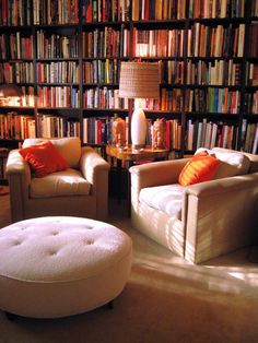 two chairs and a ottoman in front of a bookshelf with many books on it