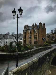 an old stone bridge crossing over a river in front of a large brick building on the other side