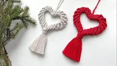 two crocheted heart ornaments hanging from a pine tree with red and white tassels