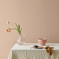 a table topped with a pink vase filled with flowers next to a plate and bowl