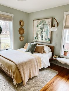 a bed sitting in a bedroom next to two windows with pictures on the wall above it