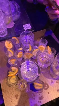 many glasses and lemons are on a table with purple lights in the room behind them