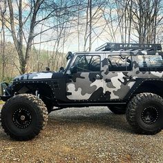 a black and white camo jeep parked in front of some trees with no leaves on it