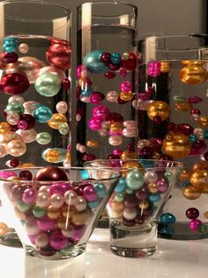 some glass vases filled with different colored balls and beads on a counter top next to each other