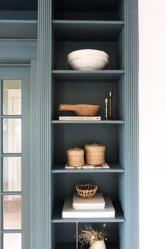 a blue bookcase filled with books next to a white bowl and other items on top of it