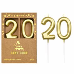 two cake candles with the numbers twenty and twenty on them in gold foil, sitting next to a cardboard box