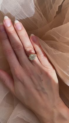 a woman's hand with a diamond ring on her left hand and veiled fabric in the background