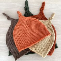 four crocheted hats on top of each other, one with an orange and the other brown