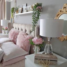 a bed with pink pillows and flowers on top of it next to a white nightstand