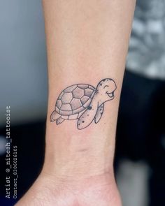 a small turtle tattoo on the wrist is shown in black and grey ink, with an outline