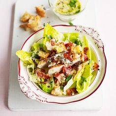 a white plate topped with lettuce covered in meat next to a bowl of sauce