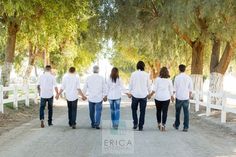 a group of people walking down a dirt road next to trees on either side of a white fence