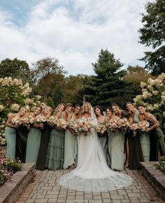 a group of women standing next to each other in front of trees and flowers on a brick walkway