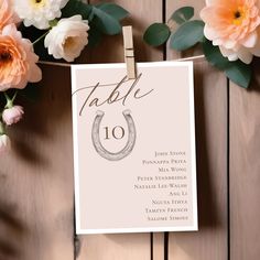 a table number card with a horseshoe on it next to some flowers and paper clips