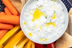 a bowl of dip surrounded by carrots and crackers