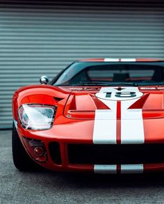 a red sports car with white stripes parked in front of a garage door on the street