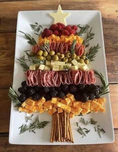 a christmas tree made out of different types of food on a white platter with olives, pineapples and berries