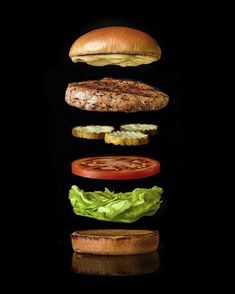 a hamburger with lettuce, tomato and cheese falling into the air on a black background