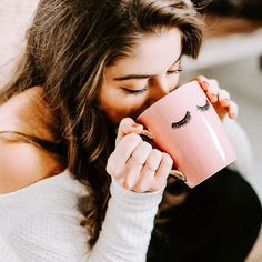 a woman holding a pink coffee mug with eyelashes on it