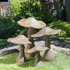 three stone mushrooms sitting on top of green grass in front of a tree and bushes