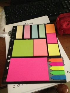 a notebook with colored sticky notes on top of it and a computer keyboard in the background