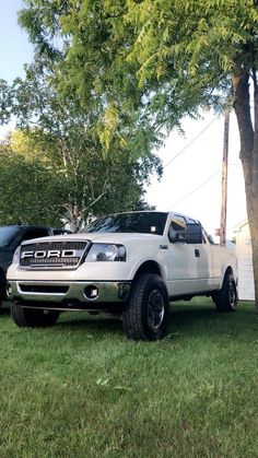 a white truck parked in the grass next to a tree